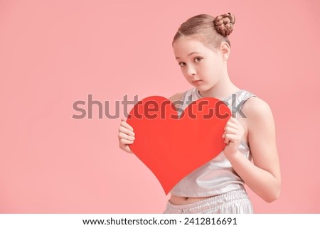 Valentine's Day concept. Pretty teenage girl poses emotionally with a red heart on a pink studio background. Copy space.