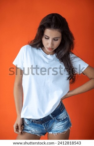Beautiful brunette girl in a white T-shirt and denim shorts posing on an orange background