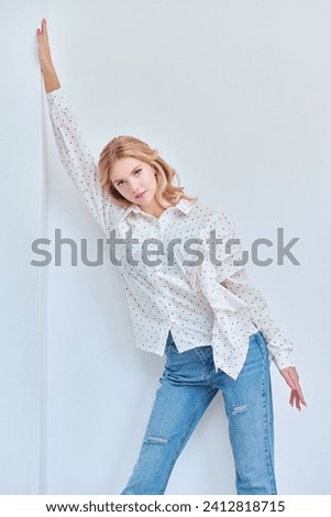 Feminine beauty. Portrait of a cute blonde girl with delicate pink makeup posing in an elegant white blouse on a pink studio background. Hairstyles, Hollywood wave.