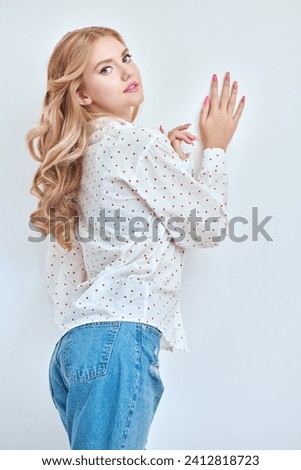 Portrait of a cute blonde girl with delicate pink makeup posing in an elegant white blouse on a pink studio background. Hairstyles, Hollywood wave. Feminine beauty. 
