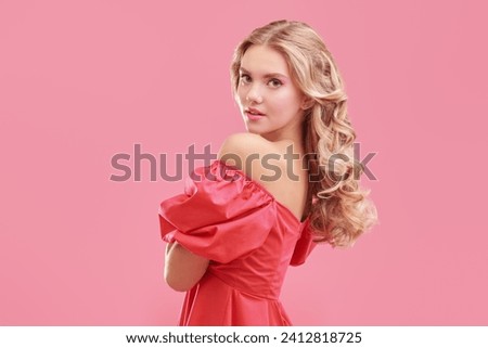 Feminine beauty. Portrait of a cute blonde girl with delicate pink makeup posing in an elegant pink dress on a pink studio background. Copy space. Hairstyles, Hollywood wave.