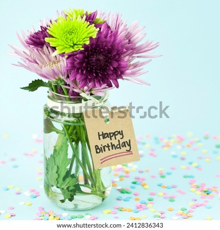 The image is a vase with purple flowers. The content of the image says "Happy Birthday." The tags for the image are plant, flower, purple, vase, floristry, floral design, and pink.