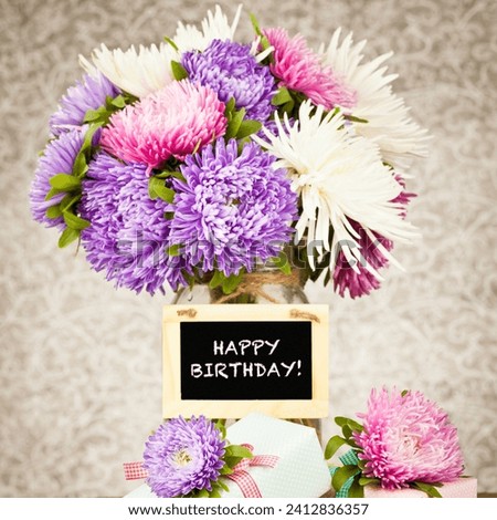 The image contains a bouquet of purple flowers arranged in a vase. It is a floral arrangement with a "Happy Birthday" message.