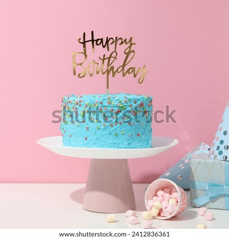 The image is a blue cake with a crown on top. It appears to be a birthday cake with the words "Happy Bartholog" written on it. The cake is placed on a cake stand and is decorated with icing and sugar 