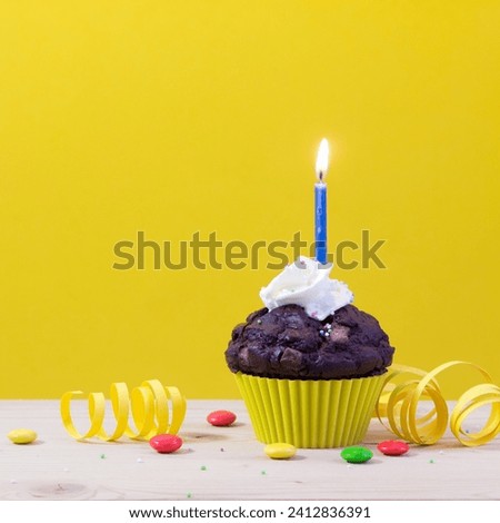 The image is of a cupcake with a candle on top, suggesting it is a birthday cake. The cupcake appears to be decorated with cream and icing, and it is placed in a baking cup.