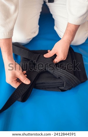 Martial arts background. Aikidoka hands folding a black traditional hakama on a blue background. Royalty-Free Stock Photo #2412844591