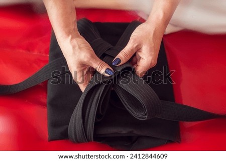 Martial arts background. Aikidoka hands folding a black traditional hakama on a red background. Royalty-Free Stock Photo #2412844609