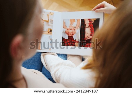 mother and daughter flips through a photo book with photos of dad and pregnant mom. Beautiful memory. Professional photo printing. services of photographer and designer. original gift for the family.