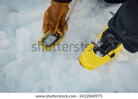 Person holding a modern avalanche beacon in his hands. Off piste skier displaying avalanche beacon and how to use it. Lavine prevention device, beacon to find a person gliding on snow. Royalty-Free Stock Photo #2412860975