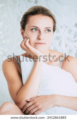 Beauty skin care young caucasian girl sitting in bed at home smile and look with blue eyes and blonde hair - relax indoor activity and beautiful female people alone in morning wake up