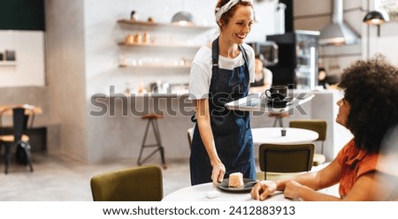 Restaurant waitress smiling and giving her customer a friendly greeting as she brings her food on a tray. Female barista serving a woman a cup of coffee and a piece of cake in a cafe. Royalty-Free Stock Photo #2412883913