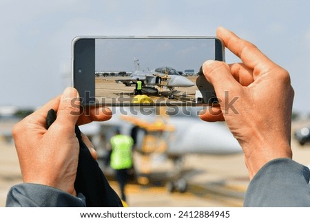 Young man hand holding Mobile phone to take a Photo air craft military on ground in airshow 