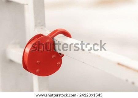 Heart-shaped red lovelock hanging on a bridge on white blurred background. Valentine's Day background. Concept Padlocks Love forever. 