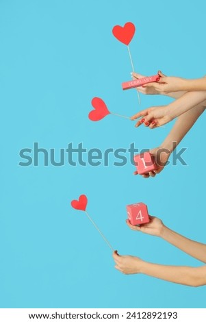Female hands holding paper hearts and cube calendar with date 14 FEBRUARY on blue background. Valentine's Day celebration Royalty-Free Stock Photo #2412892193