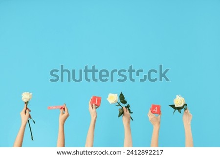 Female hands holding roses and cube calendar with date 14 FEBRUARY on blue background. Valentine's Day celebration Royalty-Free Stock Photo #2412892217