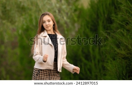 A young smiling girl walking in an autumn park in a good mood. Teenage girl, portrait against a background of nature. Fashion style trend.
