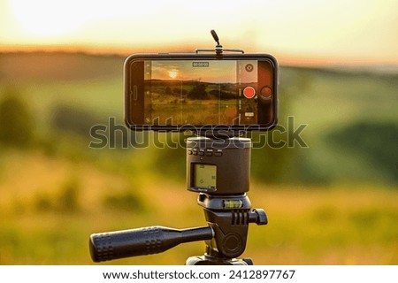 Mobile phone, smartphone on a tripod films the Beautiful sunset panorama over steppe-like landscape in Transylvania, with grasses, trees and mountains in the background, Hunedoara, Romania