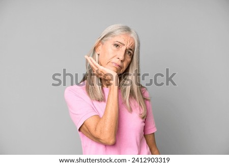 pretty gray hair senior woman feeling bored, frustrated and sleepy after a tiresome, dull and tedious task, holding face with hand
