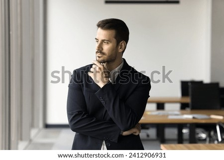 Thoughtful handsome manager man in formal suit posing in office, touching chin, looking away in deep thoughts, planning future project, thinking on business success, work ideas Royalty-Free Stock Photo #2412906931