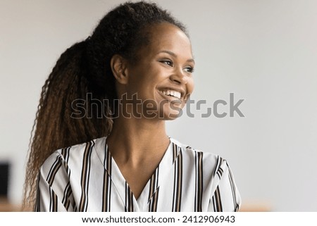 Cheerful beautiful young African American woman posing indoors, looking away with perfect toothy smile, laughing. Happy pretty female business professional girl candid portrait.