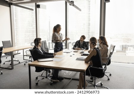 Confident young African American project manager presenting management strategy, standing at meeting table, talking to team, explaining teamwork plan, work tasks Royalty-Free Stock Photo #2412906973