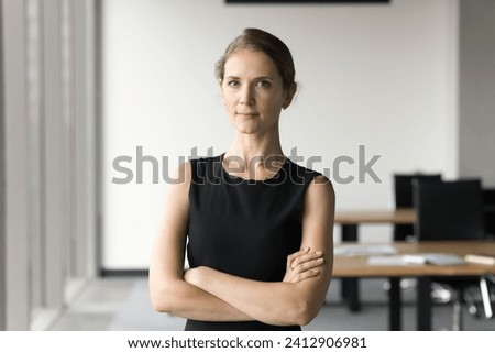 Serious attractive young businesswoman posing in office space with hands folded, looking at camera. Confident female professional, small business owner, successful company leader head shot portrait