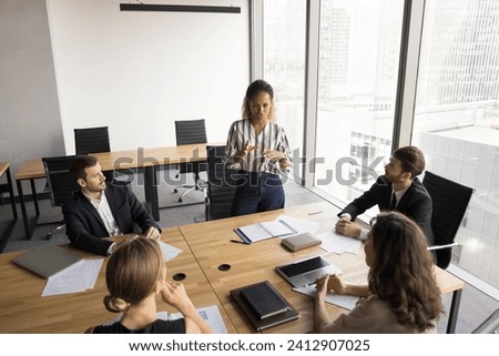 Serious young African American professional woman talking to business partners on partnership meeting, presenting startup, project plan, standing at table, speaking Royalty-Free Stock Photo #2412907025