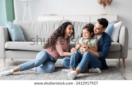 Middle Eastern Parents Having Fun With Their Little Daughter At Home, Arabic Mom And Dad Tickling Female Kid And Laughing Together In Living Room, Enjoying Domestic Leisure, Copy Space Royalty-Free Stock Photo #2412917927