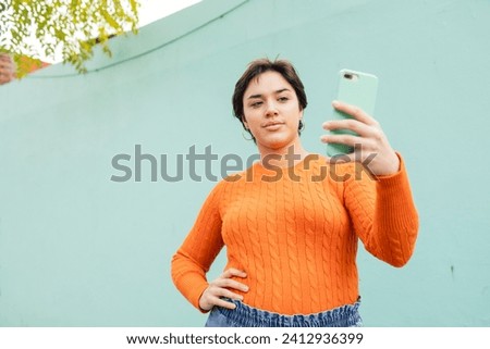 Young woman taking selfie through smartphone against turquoise wall