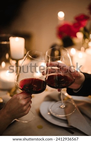 Couple in love drinking wine. Cheers. Romantic date by candlelight at night. Hands man and woman hold glasses at home. Toast. Dinner setup table for couple on Valentine's day. Proposal hand and heart. Royalty-Free Stock Photo #2412936567