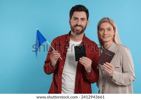 Immigration. Happy couple with passports and flag of European Union on light blue background Royalty-Free Stock Photo #2412943661