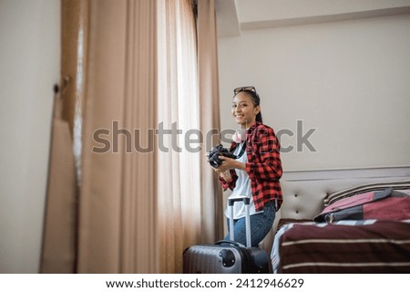 smiling female local tourist holding a camera to take pictures from the hotel room window