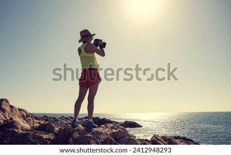 Woman taking photo on sunrise seaside rocky mountains
