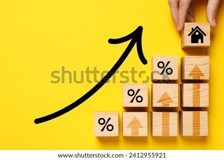Mortgage rate rising illustrated by upward arrows. Woman putting wooden cube with house icon near other ones on yellow background, top view