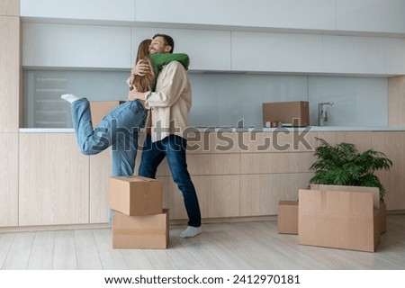 Overjoyed wife and husband hugging on kitchen moving to new flat among cardboard boxes. Relocation, family mortgage, buying apartment, real estate. Happy emotional couple spouses enjoying life changes Royalty-Free Stock Photo #2412970181