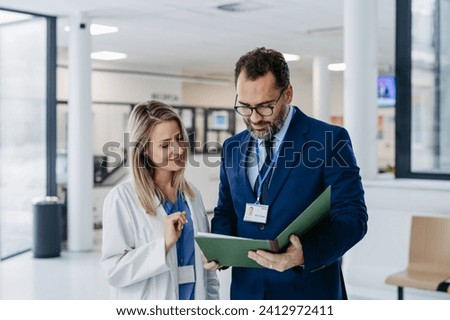 Pharmaceutical sales representative talking with doctor in medical building. Female doctor talking with hospital director, manager in private clinic. Royalty-Free Stock Photo #2412972411