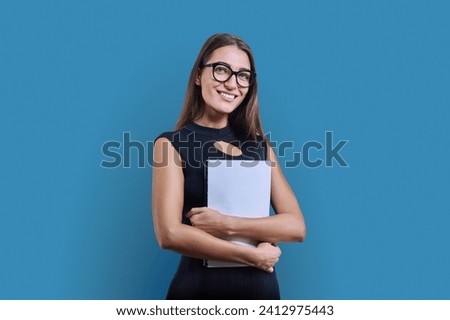 Young business woman with clipboard looking at camera on blue background Royalty-Free Stock Photo #2412975443