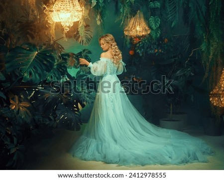 Art photo real person Fantasy woman walking in room greenhouses indoor plants Tropical trees green leaves . Fairy tale Girl princess back rear view long blond hair. luxury blue lush dress old style.