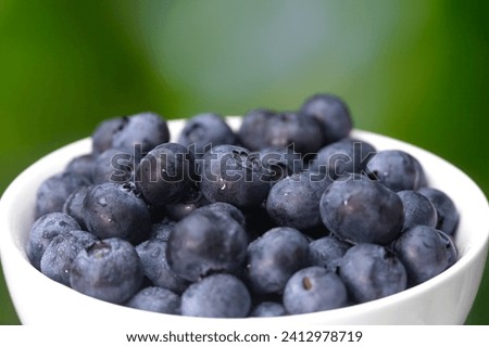 Close-up of a white bowl with blueberries on a blurry green background, macro photography