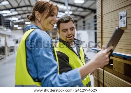 Young man with Down syndrome working in warehouse, female colleague teaching him scan products with scanner. Concept of workers with disabilities, support in workplace. Royalty-Free Stock Photo #2412994529