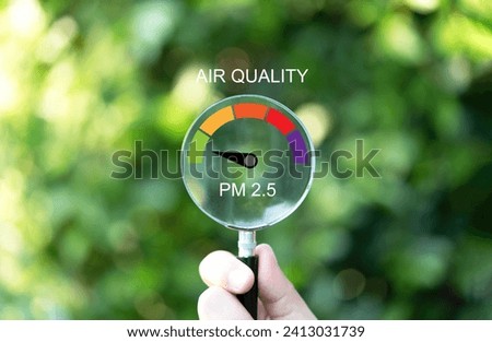 Hand holding magnifier glass with good air quality indicator scale on greenery background which check PM 2.5 or particulate matter 2.5 micron for air pollution effect to health and lifestyle concept. Royalty-Free Stock Photo #2413031739