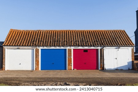 Block of four garages with coloured doors with a tiled roof. Suffolk. UK Royalty-Free Stock Photo #2413040715