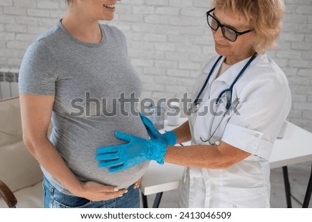Pregnant woman visiting a doctor. Elderly Caucasian female gynecologist holds hands on the tummy of a pregnant patient. 