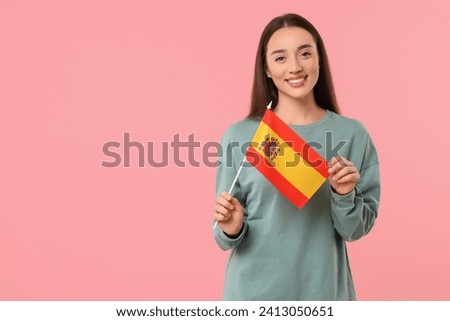 Young woman holding flag of Spain on pink background, space for text