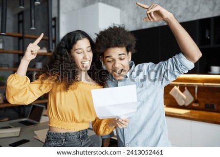 Happy excited african american young couple feeling euphoric while reading paper letter with positive bank response on their mortgage request, yelling and putting index finger up with overjoyed faces Royalty-Free Stock Photo #2413052461