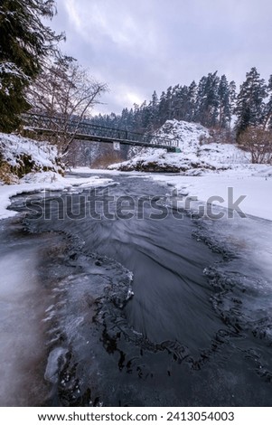 Half-frozen Hornad river with rapids in winter at sunset Slovak Paradise. An iron bridge over a frozen river. Discovering the beauty of the winter landscape. Royalty-Free Stock Photo #2413054003