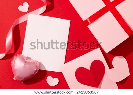 Top view of pink cards, paper hearts, a heart-shaped balloon and ribbons are decorated on a red background. Design space with Valentine's Day theme. Royalty-Free Stock Photo #2413063587