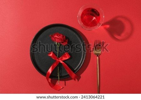 Top view of a ceramic dish in black color with a rose placed on. A golden fork and a red wine glass featured. Concept for Valentine party