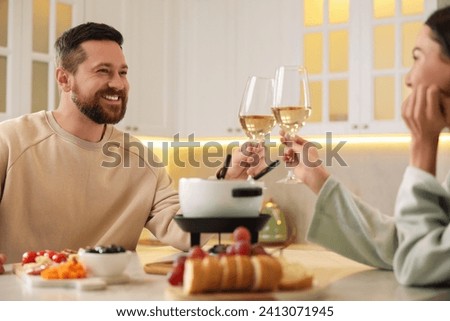 Romantic date with fondue. Couple clinking glasses of wine at home