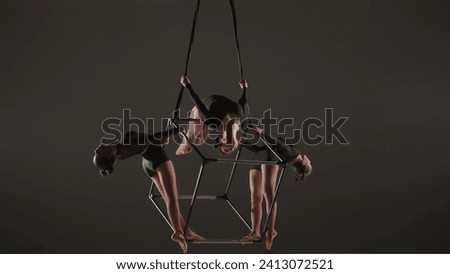 Portrait of female acrobats isolated black background. Girls aerialists dancers trio holding spinning in the air on cube with ropes.